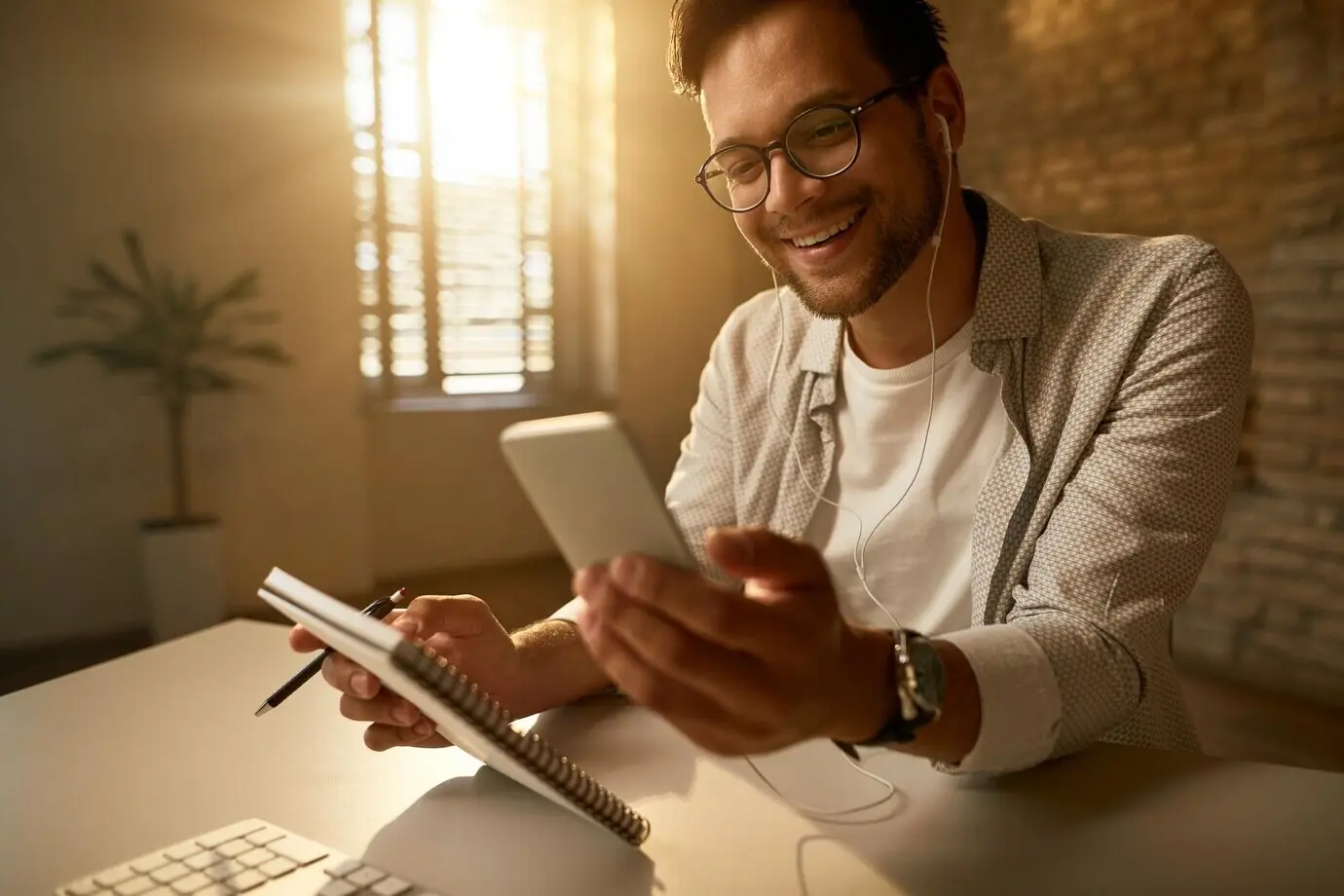 A happy young freelance worker reads a text message on a mobile phone while working in the office.